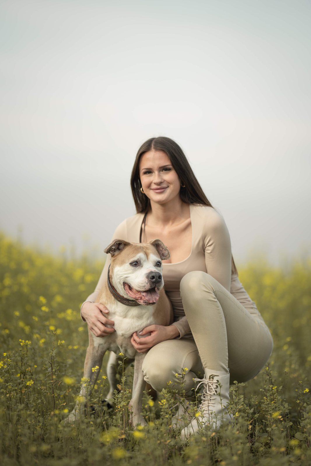 Frau kniet lächelnd mit ihrem Hund im Blütenfeld